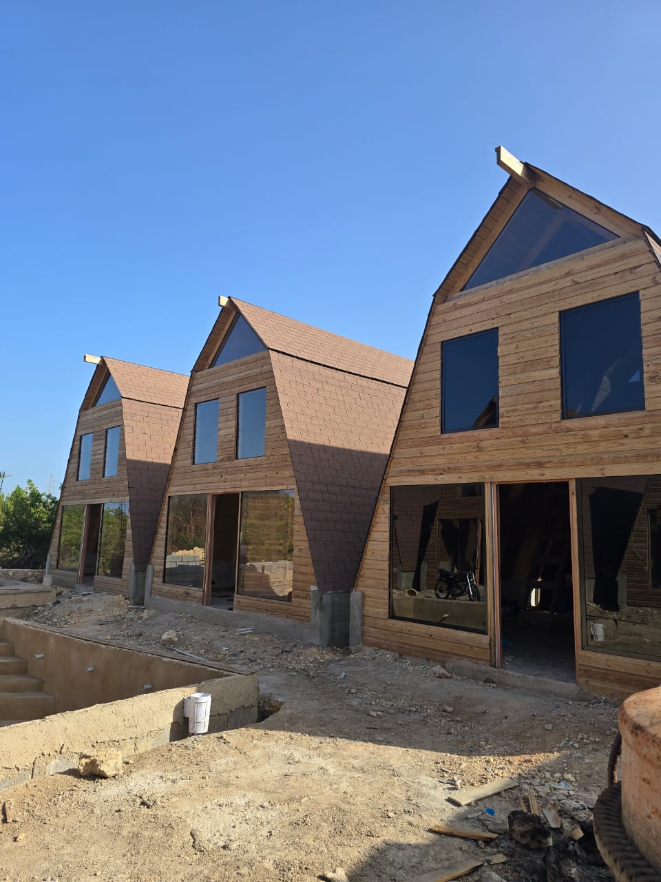 Wooden A-frame eco cabins with tall glass windows under a blue sky